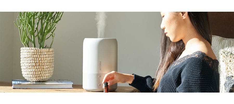 Woman reading essential oil label as she places the bottle near diffuser