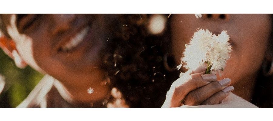 Couple outside blowing on a dandelion in spring