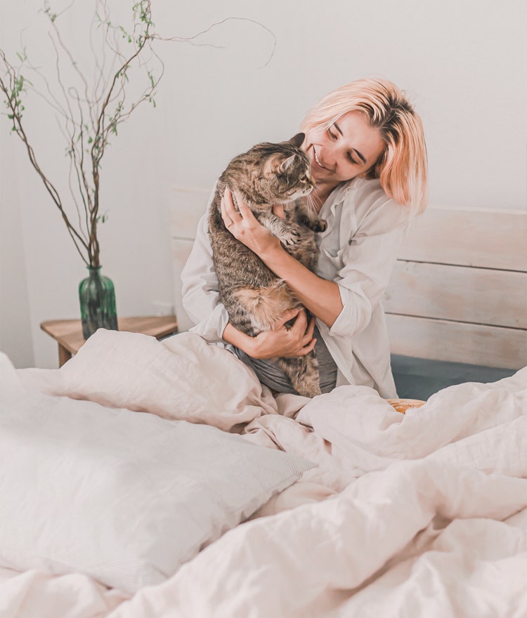 Happy, relaxed woman sitting up in bed and cuddling her cat