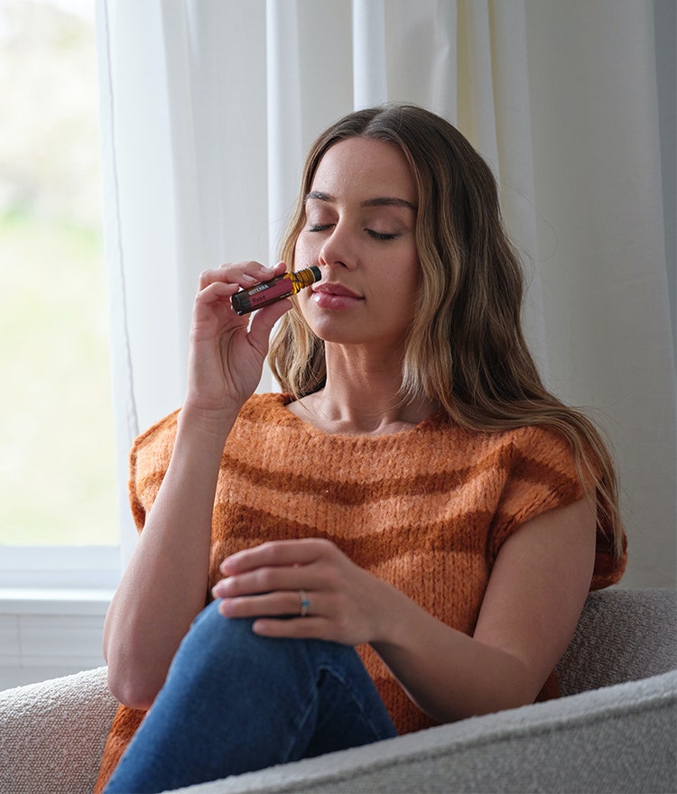 Woman sitting near window and smelling a bottle of essential oil