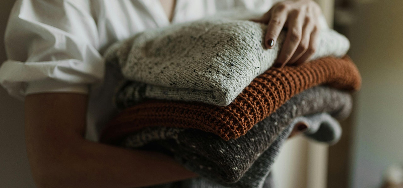 woman holding a stack of folded sweaters