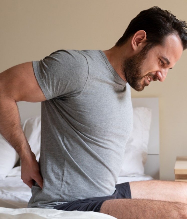 man with back pain sitting on firm mattress