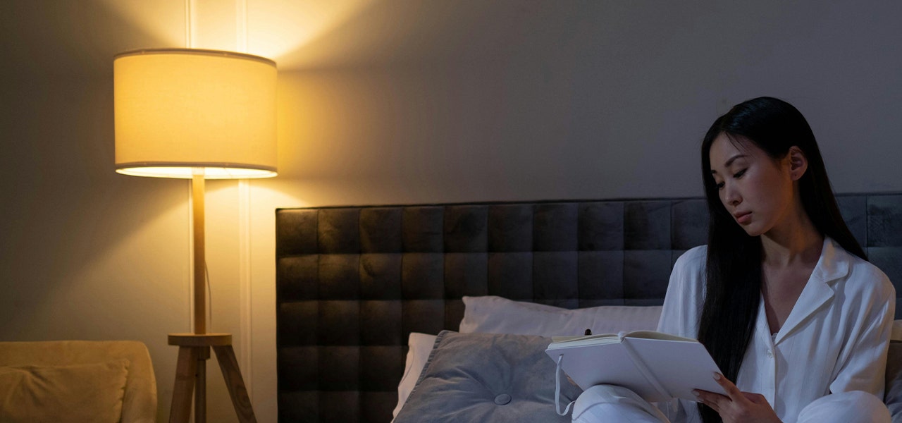 woman sitting in bed with bedside lamp turned on