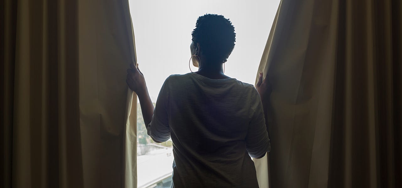 woman standing in window with dark colored drapes