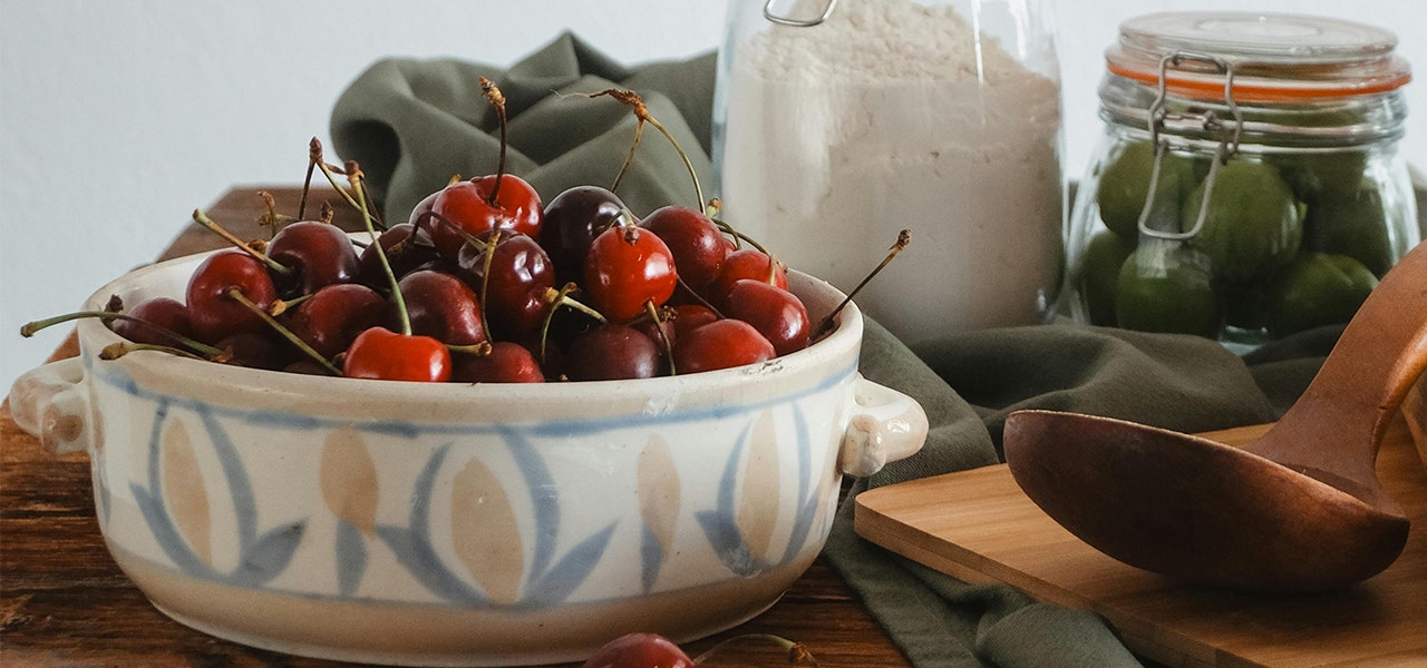 bowl of cherries next to jars of other provisions