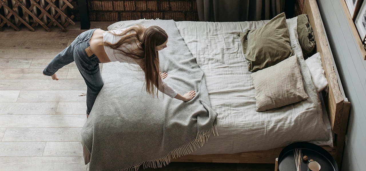 person putting a blanket on a bed