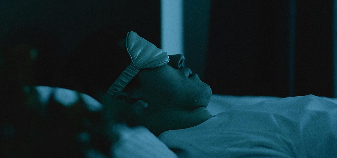 person laying in bed at night wearing eye mask